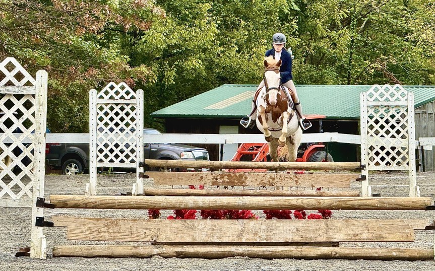 A paint horse and her little girl rider go over a jump.